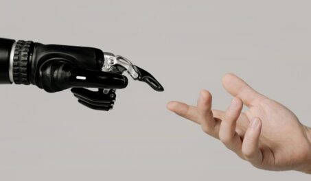 A human hand reaching to touch a bionic prosthetic hand on a white background.